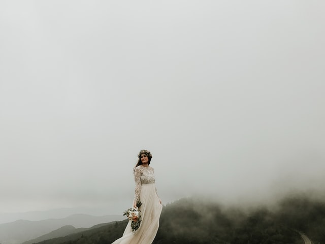 "A bride is standing with a bouquet in her hand on the top of a hill"